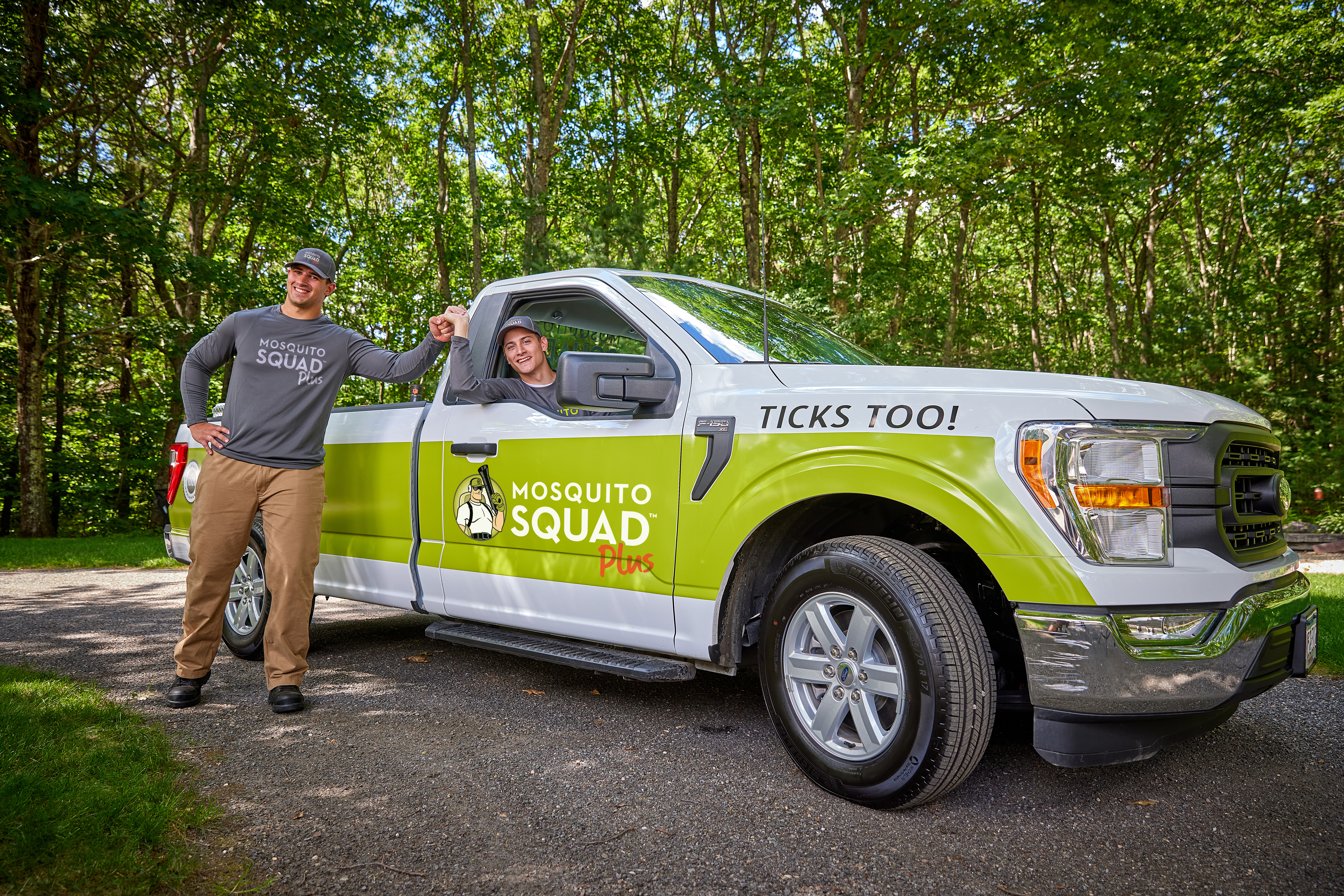 Two Mosquito Squad team members smiling in front of and inside a branded truck